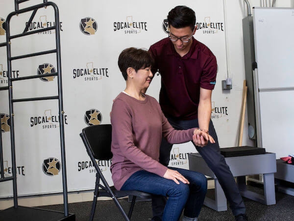 Male physical therapist aiding a woman's left arm and elbow