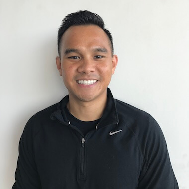 Man with short dark hair and dark jacket smiling against a white wall